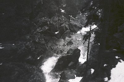 Black-and-white aerial view of a densely packed urban area with grid-like streets and industrial structures. Shadows and ligh...