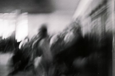 Blurred monochrome shot capturing motion blur of a crowd in an indoor setting, likely a public event or gathering. Soft focus...