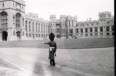 Black-and-white shot of a sentry in traditional British military uniform (helmet, sash, boots) standing at attention outside ...