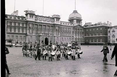 Military band performing in front of Buckingham Palace courtyard, mid-20th century. Uniformed musicians in white tunics and d...