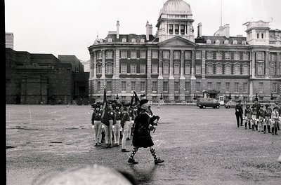 Neoclassical government building with symmetrical columns and domed roof, flanked by uniformed guards in traditional kilts an...