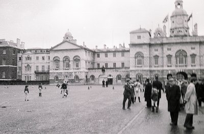 Neoclassical courtyard with grand, symmetrical buildings featuring arched windows and domed roofs. Mid-20th century street sc...