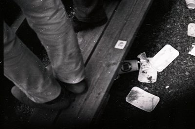 Black-and-white close-up of a person’s legs stepping over discarded soap bars on a metal rail. Industrial or institutional se...