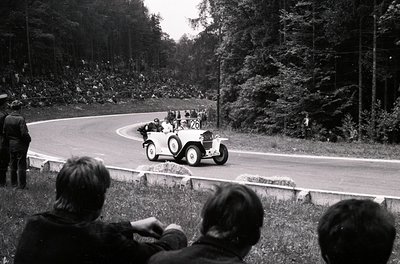 Vintage open-top race car () navigating a winding forest road during a rally, surrounded by spectators. Classic 1930s–1950s a...