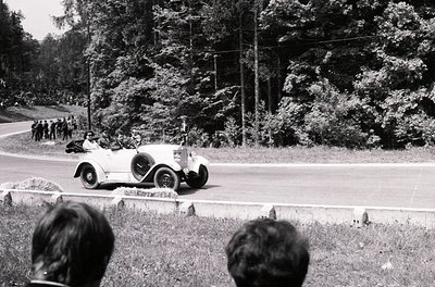 Classic 1930s roadster racing on a rural road, surrounded by spectators. Open-top vintage car with streamlined bodywork and w...