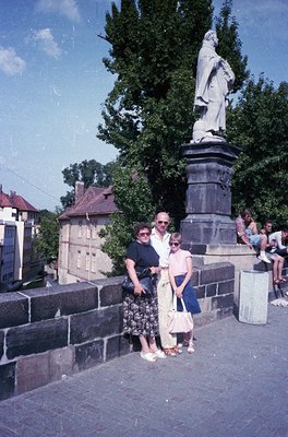 Family poses on a stone bridge beside a statue of a robed figure, likely a historical or religious monument. Mid-20th century...