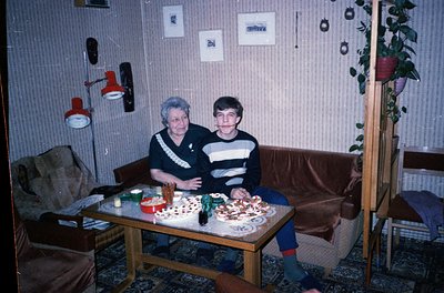 Vintage indoor portrait of two generations seated at a wooden table with homemade baked goods. Woman in striped sweater, man ...
