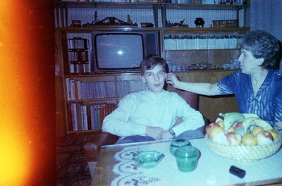 Vintage indoor scene featuring a young boy and adult woman in a mid-century living room. Wooden bookshelves filled with vinyl...