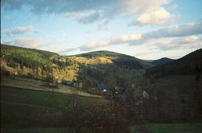 Vintage landscape shot of rolling hills with autumn foliage, sparse farmhouses, and dense forest. Soft color tones suggest mi...