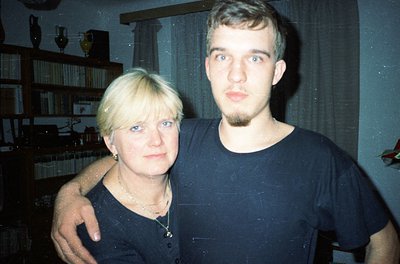 Vintage portrait of a woman and young man in a dimly lit indoor setting, likely 1980s–1990s. Woman wears a dark top with a pe...