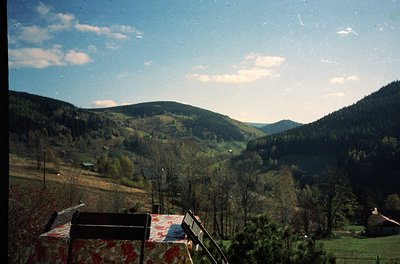 Vintage landscape shot of a valley with rolling hills, sparse forest, and scattered farmhouses. Foreground features a pattern...