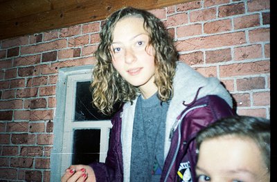 Vintage candid shot of two individuals peeking through a brick archway, likely 1980s–1990s. The person in focus wears a layer...
