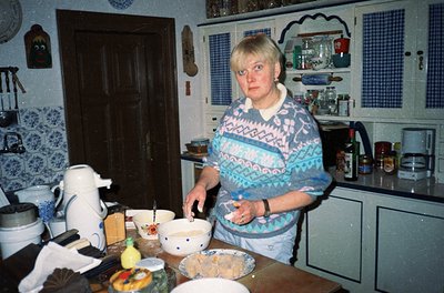 Mid-century kitchen scene featuring a woman in a patterned sweater and light-colored apron preparing food on a wooden counter...