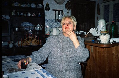 Vintage kitchen scene featuring a woman in a textured sweater, seated at a table adorned with a blue-and-white tablecloth. Sh...