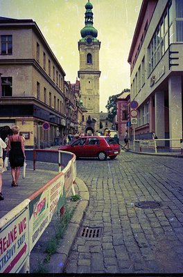 Vintage street scene featuring a cobblestone road leading to a prominent **18th-century bell tower** with a green dome, likel...
