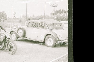 Vintage black-and-white photo of a classic 1930s–1940s roadside scene: a closed-couple car (likely a Ford or Chevrolet) parke...
