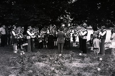 A mid-20th century funeral procession with a brass band playing at gravesites. Uniformed musicians in 1950s-60s attire, inclu...