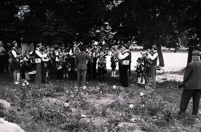 Group of musicians in outdoor setting playing brass instruments at a graveside ceremony, likely mid-20th century. Uniformed f...