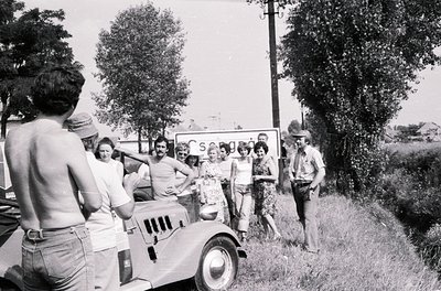 Vintage black-and-white photo of a group posing with a vintage truck, likely 1960s–1970s. Casual summer attire (shorts, hats)...