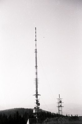 Mid-20th century communications tower with spherical antennas, set against forested hills. Likely a Cold War-era military or ...