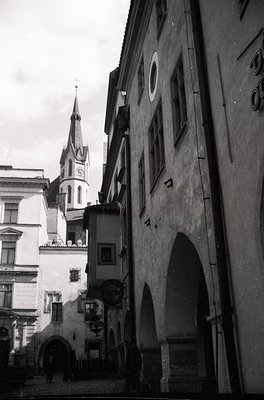 Black-and-white street scene featuring Gothic Revival architecture. Prominent church spire with ornate detailing and clock to...