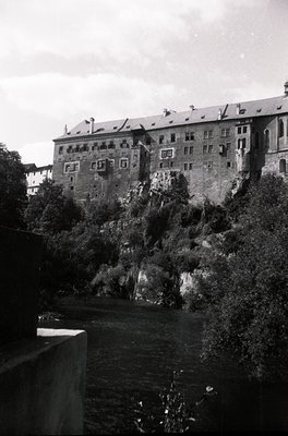 Historic castle perched on rocky cliffs beside a river, featuring symmetrical brick architecture with numerous windows and ch...