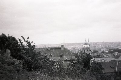 Vintage black-and-white urban panorama featuring a domed church with a tall spire in the background, surrounded by low-rise b...
