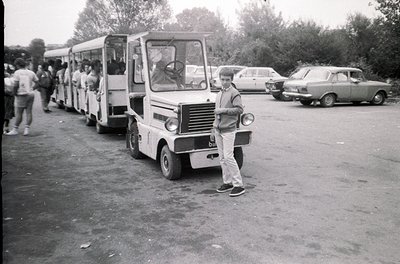 Vintage microbus parked in a lot, likely Eastern Bloc-era design. A man in 1970s-style casual wear (sneakers, baggy pants, sh...
