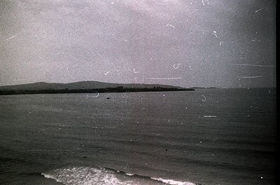 Vintage black-and-white seascape with low-contrast coastal landscape and gentle waves. Minimalist horizon line separates land...