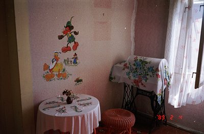 Vintage room featuring 1950s–60s Disney mural of Donald Duck, Mickey Mouse, and Goofy on faded wall. Round floral-patterned t...