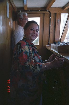 Vintage train interior with two passengers: woman in floral-patterned blouse and man in white shirt, seated near wooden-panel...