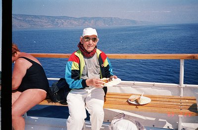 Retro cruise deck scene: man in 1990s-style safety vest, white cap, and sunglasses holding a plate with a sandwich, seated on...