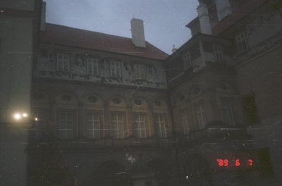 Neoclassical courtyard building with intricate stone reliefs and arched windows, captured through rain-streaked glass. Date s...