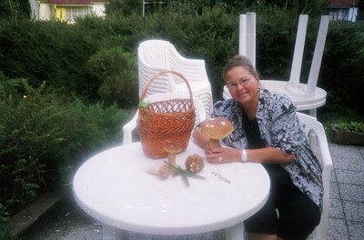 Mid-2000s outdoor café scene featuring a woman in a patterned blouse posing beside a white plastic table. Table holds a woven...