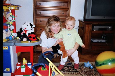 A woman and toddler pose indoors in a mid-20th-century home, likely 1980s–1990s. The woman holds the child in a light green s...