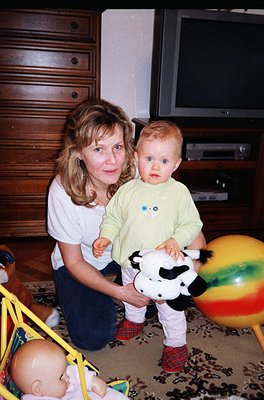 A woman and toddler pose indoors, likely mid-1990s. The woman holds a black-and-white cow plush toy, while the child wears a ...