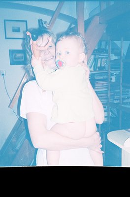 Vintage sepia-toned photo of an adult holding an infant indoors, likely mid-20th century. The adult wears a sleeveless top, a...
