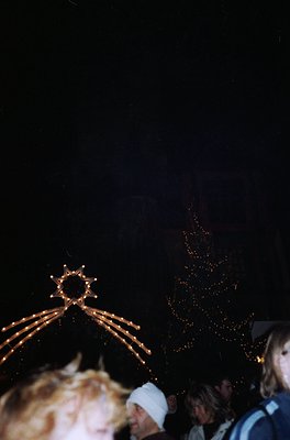 Blurred nighttime festive scene with illuminated tree and decorative arch. Warm golden lights contrast against dark backgroun...