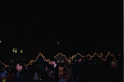 Vintage nighttime street scene with neon light trails from moving vehicles, capturing motion blur. Crowd of casually dressed ...