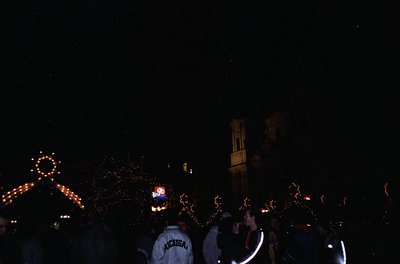 Nighttime crowd celebration with illuminated star decorations and a clock tower silhouette. Two individuals in Michigan-theme...