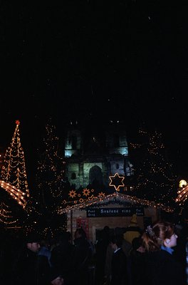 Nighttime festive scene featuring illuminated Christmas decorations. A large, ornate tree adorned with warm lights and star o...