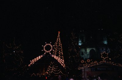 Vintage-style nighttime holiday display featuring illuminated Christmas tree, star, and menorah-inspired lights. Architectura...