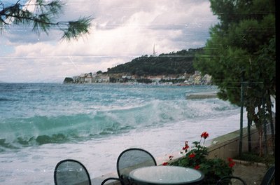 Seaside view through vintage glass patio doors, featuring crashing waves on a rocky coastline. Metal patio furniture and red ...