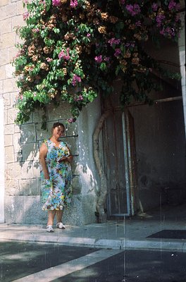 Vintage floral dress with geometric patterns stands out against blooming bougainvillea-covered wall. Concrete archway and wea...