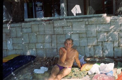 Vintage outdoor hot tub scene with a man seated in a concrete-lined pool, partially submerged in warm water. Surrounding him ...