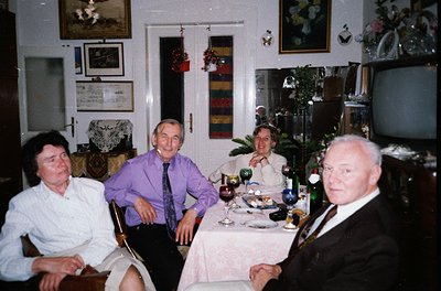 Four adults seated at a festively set dining table in a vintage interior, likely late 20th century. Formal attire (suits, tie...
