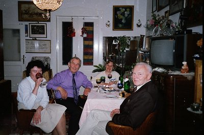 Vintage indoor gathering in a mid-century living/dining space. Four adults seated around a table with wine glasses, bottles, ...