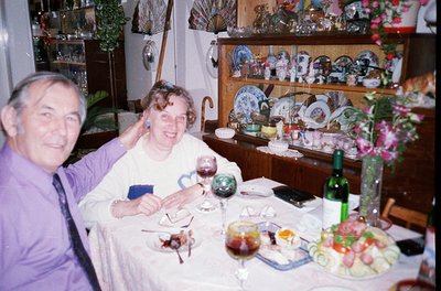 Vintage indoor dining scene featuring two adults seated at a table adorned with a spread of meats, cheeses, and wine. Wooden ...