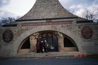 Stone archway entrance with Latin inscription *"Interfecti Mel Resurgent"* (Martyrs Rise Again) flanked by sculpted figures. ...