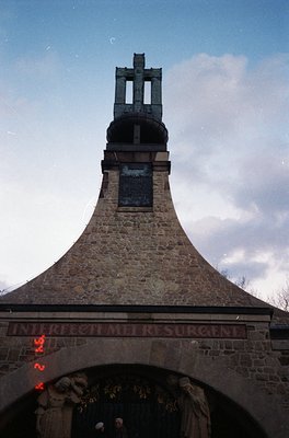 Stone bell tower with Latin inscription *"INVICTI RESURGENT"* (Latin for "The Unconquered Will Rise") and a prominent crucifi...